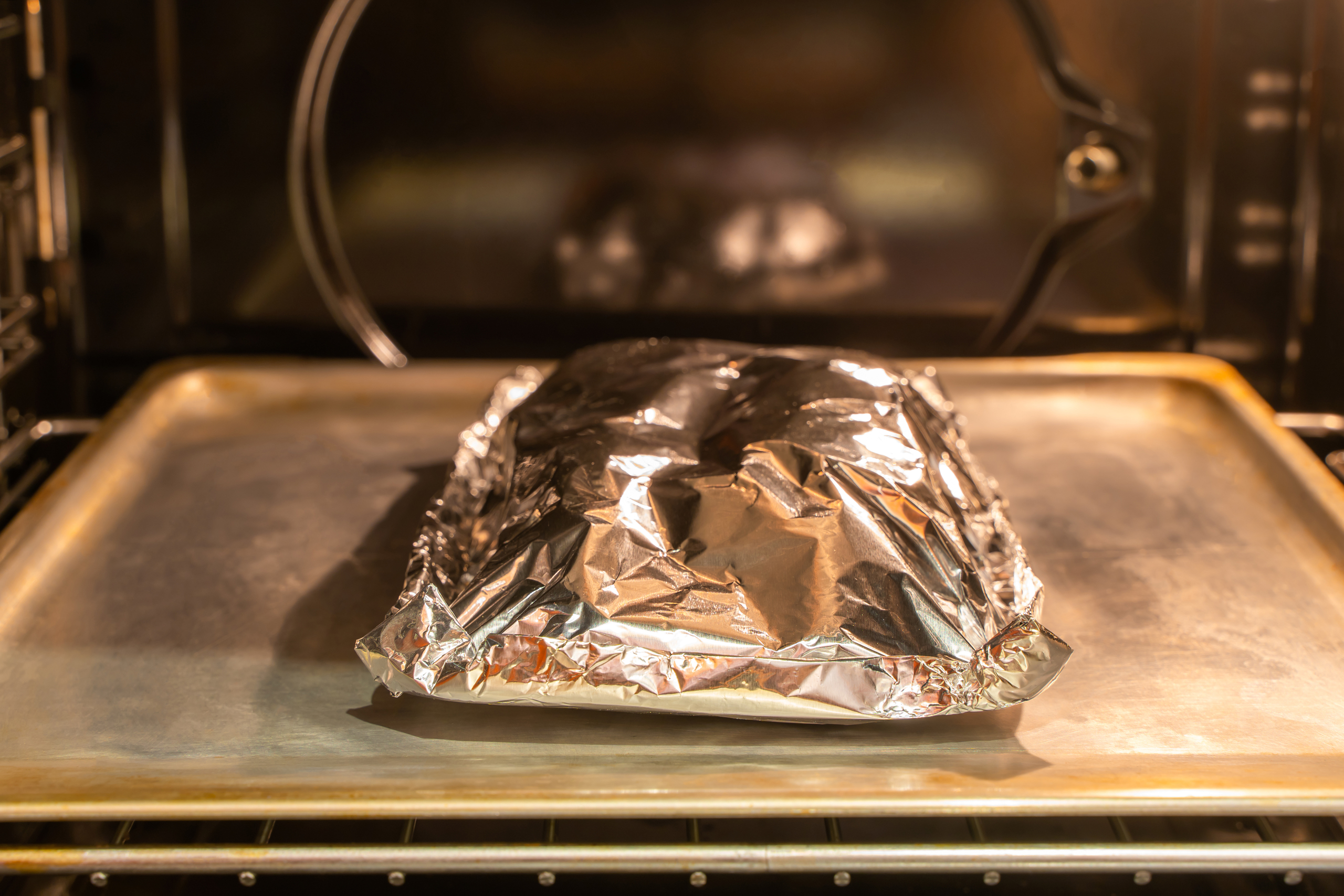 Food covered with foil on the pan inside gas oven ready for cooking. Stock photo
